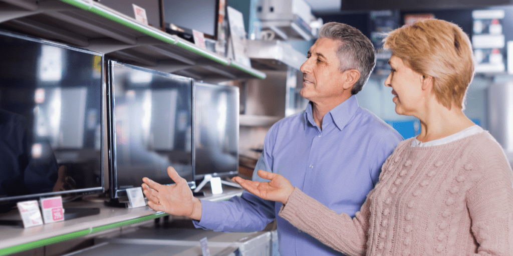 A man and woman stand in front of televisions for sale at a store.